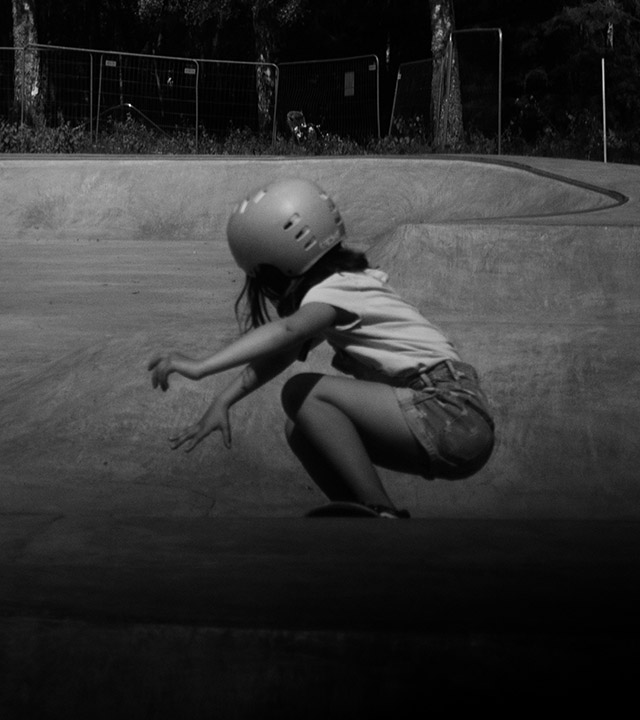 Svartvitt foto av en flicka som åker på en skateboard i en betongpark.