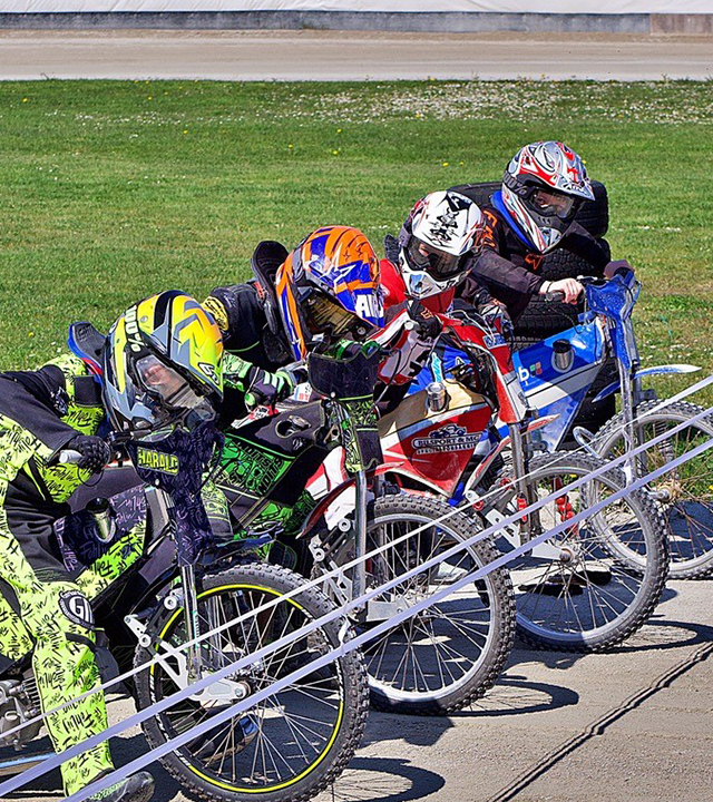 Barn på speedway-motorcyklar redo vid startlinjen.